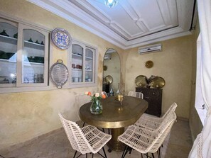 A dining area with a round table, white wicker chairs, a decorative mirror, and wall-mounted plates. - Luxurious 5-bedroom Apartment in Marrakesh With Full Accessibility (Marrakech)