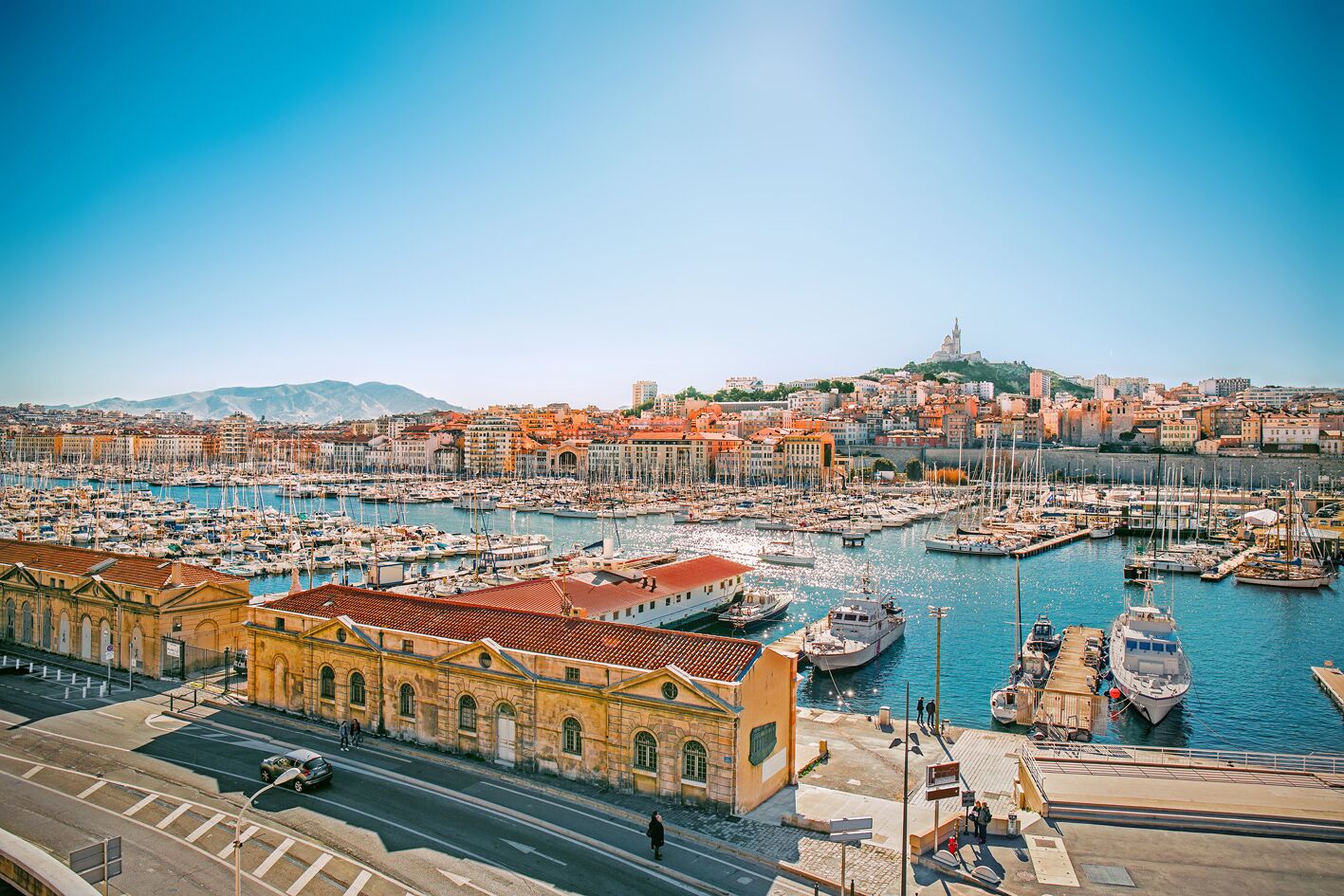 Una marina con numerose imbarcazioni, un edificio giallo ben visibile e uno skyline sullo sfondo.