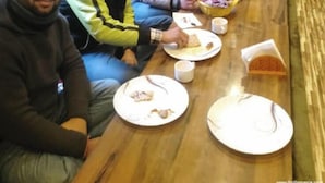 A group of people seated around a wooden dining table with plates and cups, in a room with wooden walls and a window. - Thrillomania Kasol (Kasol)