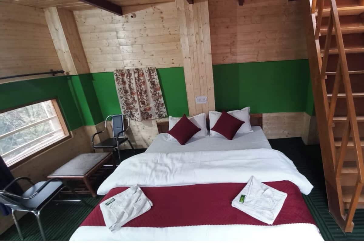 A wooden cabin room with a bed, a chair, a table, and a wooden ladder.