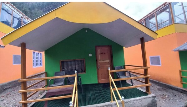Une petite pièce colorée avec un mur vert, une porte en bois et une fenêtre. On y trouve une petite table et deux chaises.