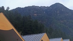 A row of cabins with metal roofs, green and red walls, and outdoor seating. - Thrillomania Kasol (Kasol)
