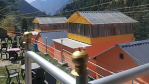 A mountainous area with several small, colorful buildings, likely guest houses or cabins, with a clear sky and distant mountains. - Thrillomania Kasol (Kasol)