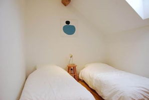 A bedroom with two beds, a wooden nightstand, a wall-mounted light, and a ceiling vent.