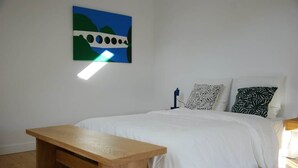 Une chambre à coucher avec un lit, un banc en bois, une lampe fixée au mur et un tableau.