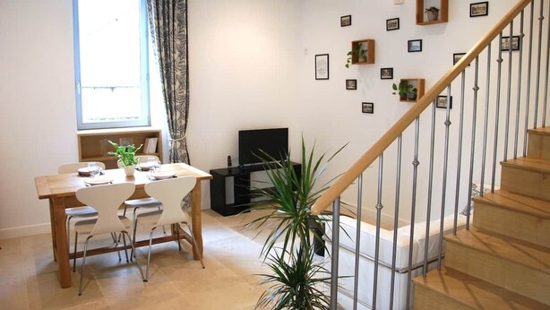 Un coin repas avec une table et des chaises en bois, une plante en pot, un escalier avec une rampe et un mur orné de tableaux encadrés.