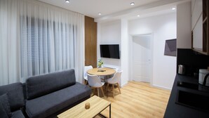 Una sala moderna con sofá, una mesa de comedor con sillas, televisor y zona de cocina.