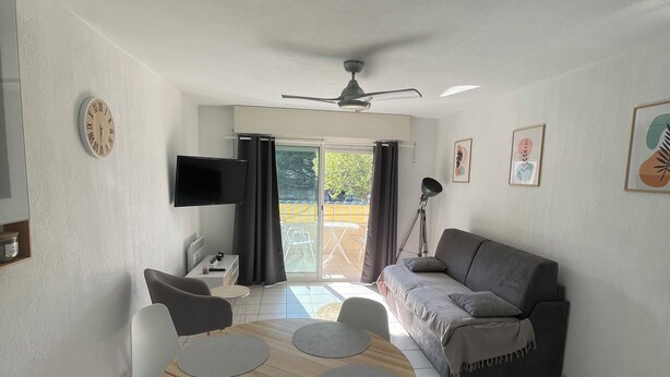 A modern living room with a ceiling fan, a flat-screen TV, a sofa, a coffee table, and a dining area with chairs. - Apt 4 pers. - swimming pool - 750 m. from the beach Private parking (Fréjus)