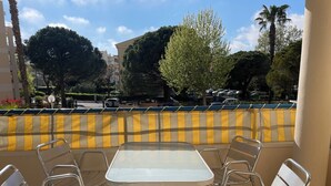 A terrace with a table and chairs, a yellow and beige checkered wall, and a view of the street and trees. - Apt 4 pers. - swimming pool - 750 m. from the beach Private parking (Fréjus)