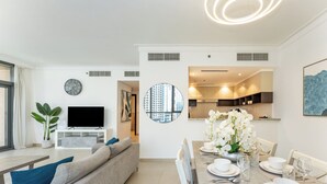 Een moderne woonkamer met een bank, televisie, eettafel voor vier personen, en een keuken die door een open deur zichtbaar is.