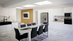 A modern kitchen with a dining area, featuring a large island, built-in appliances, and a flat-screen TV.