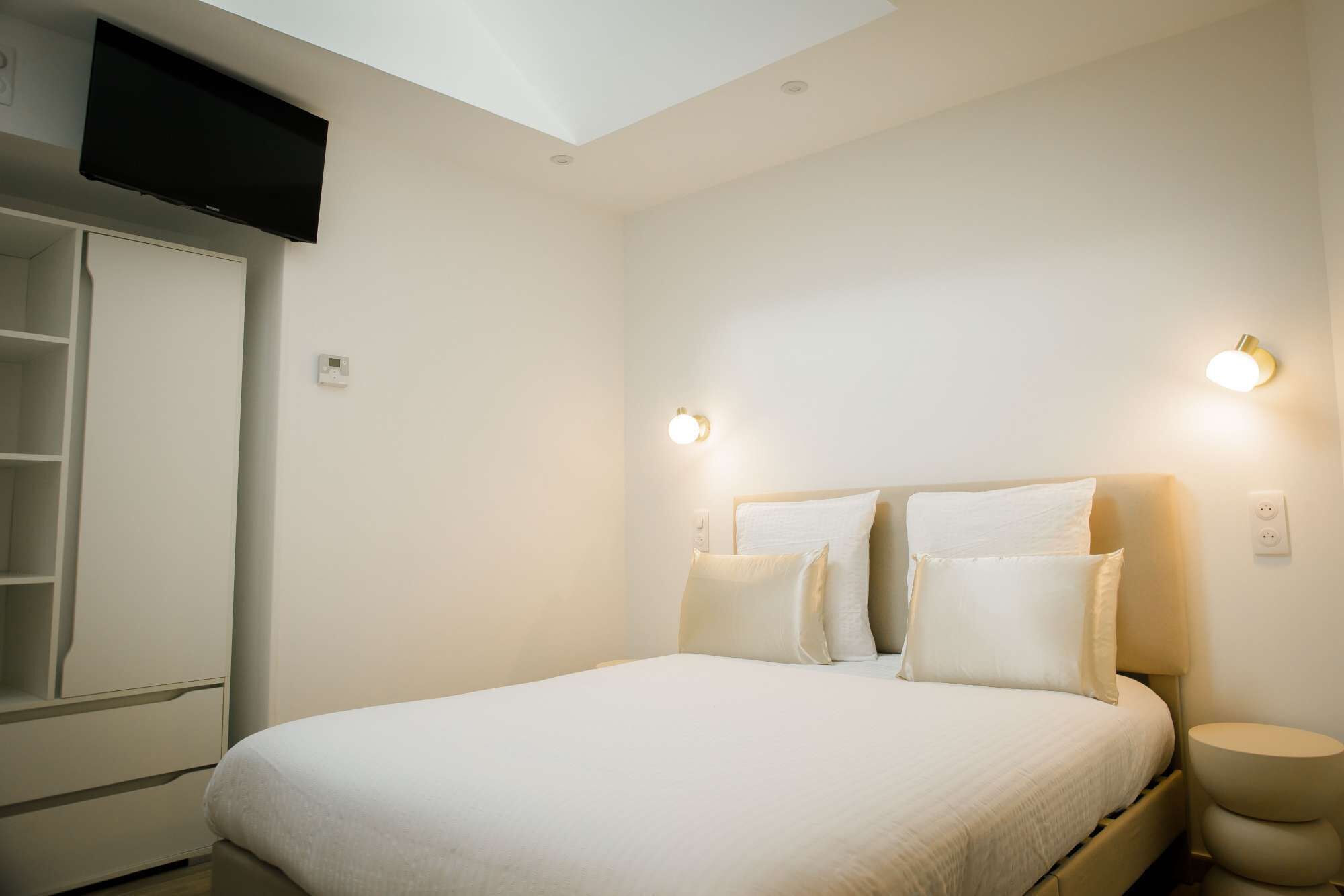 Een slaapkamer met een bed, bedlampen, een kledingkast en een aan de muur bevestigde televisie.