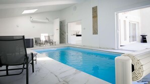 A swimming pool with a tiled deck, a lounge chair, and a door leading to a kitchen area.