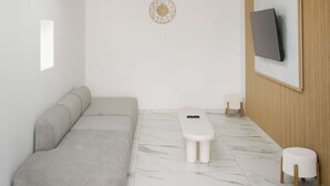 A modern living room with a sofa, a small table, a TV mounted on a wooden panel, and a skylight.