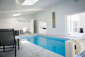 A swimming pool with a tiled deck, a lounge chair, and a door leading to a kitchen area. - L'Évéa: An Exceptional 5-Star Vacation Rental with an Indoor Pool & Spa in the Heart of Tarn-et-Garonne (Saint-Amans-du-Pech)