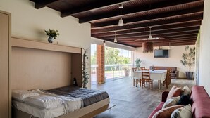 A modern room with a bed, a red couch, a dining area, and a TV. - Casa Canto: Villa with Private Heated Pool, Wi-Fi, and Air Conditioning (Estela)
