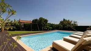 A swimming pool with lounge chairs, a wooden deck, and a house in the background. - Casa Canto: Villa with Private Heated Pool, Wi-Fi, and Air Conditioning (Estela)