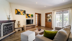 A living room with a fireplace, sofa, TV, and artwork on the wall. - Casa Canto: Villa with Private Heated Pool, Wi-Fi, and Air Conditioning (Estela)