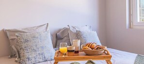 Ein Bett mit Kissen, ein Tablett mit Frühstücksgegenständen und ein Fenster.