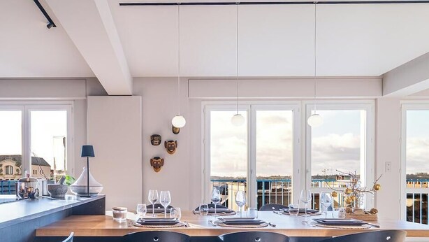 A modern dining area with a long table set for four, large windows, and a view of the cityscape.
