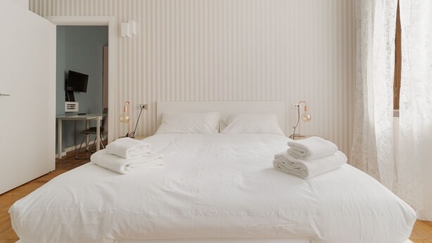 Un dormitorio blanco con cama, lámparas de noche y un escritorio con silla.