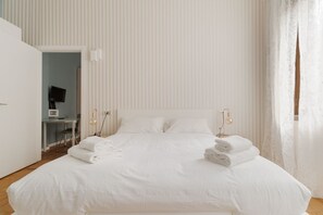 A white bedroom with a bed, bedside lamps, and a desk with a chair. - Elegant flat of 60m2, perfect for 4 people, located on the first floor with lift.The accommodation is in Missori, in the heart of Milan’s historic center, a few steps from the Duomo, near Velasca Tower and Palazzo del Novecento.Well-connected area (M3  (Milan)