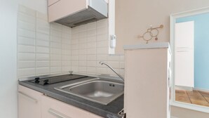 Una cocina con baldosas blancas, un lavamanos de acero inoxidable y una estufa a gas.