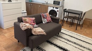 Ein kompakter Wohnbereich mit Sofa, kleinem Tisch, Waschmaschine und Mikrowelle in der Küchenzeile.