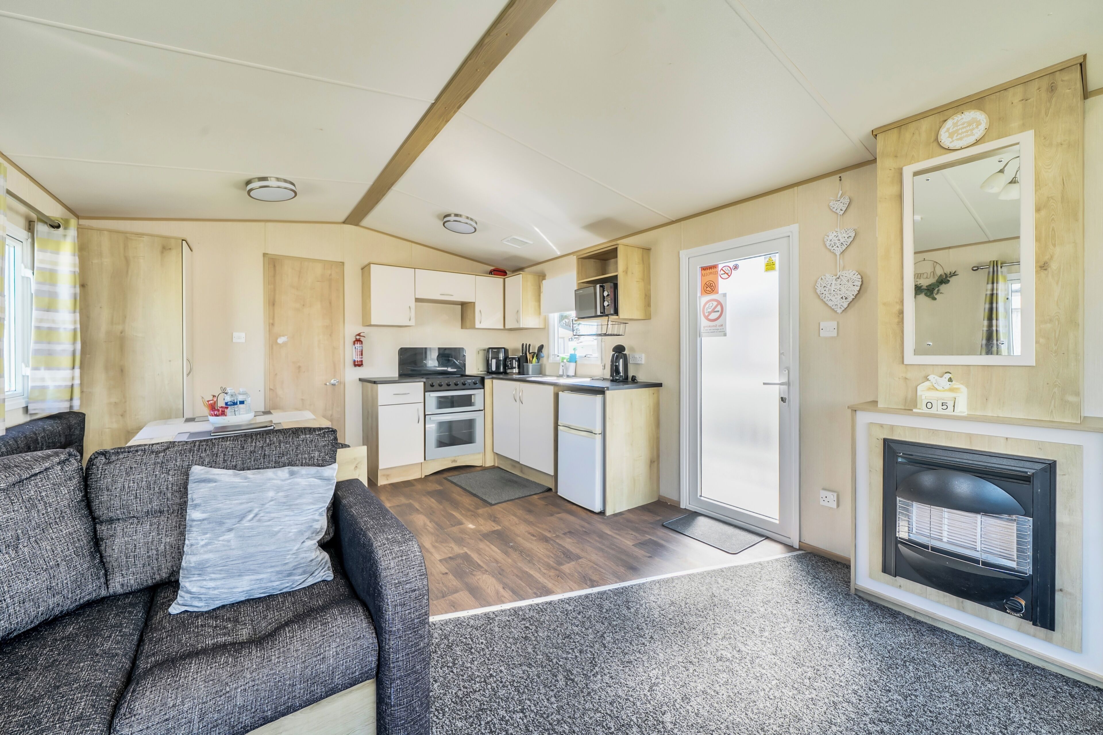 A compact RV interior with a kitchenette, a sofa, a fireplace, and a mirror.