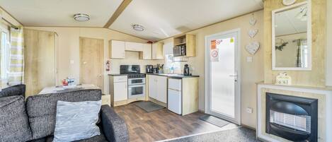 A compact RV interior with a kitchenette, a sofa, a fireplace, and a mirror.
