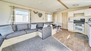 A compact living space with a sofa, a small table, a kitchen area with a stove and oven, and a window with curtains. - Sleeps 8 - Communal Spa Access - Parking (Rhyl)
