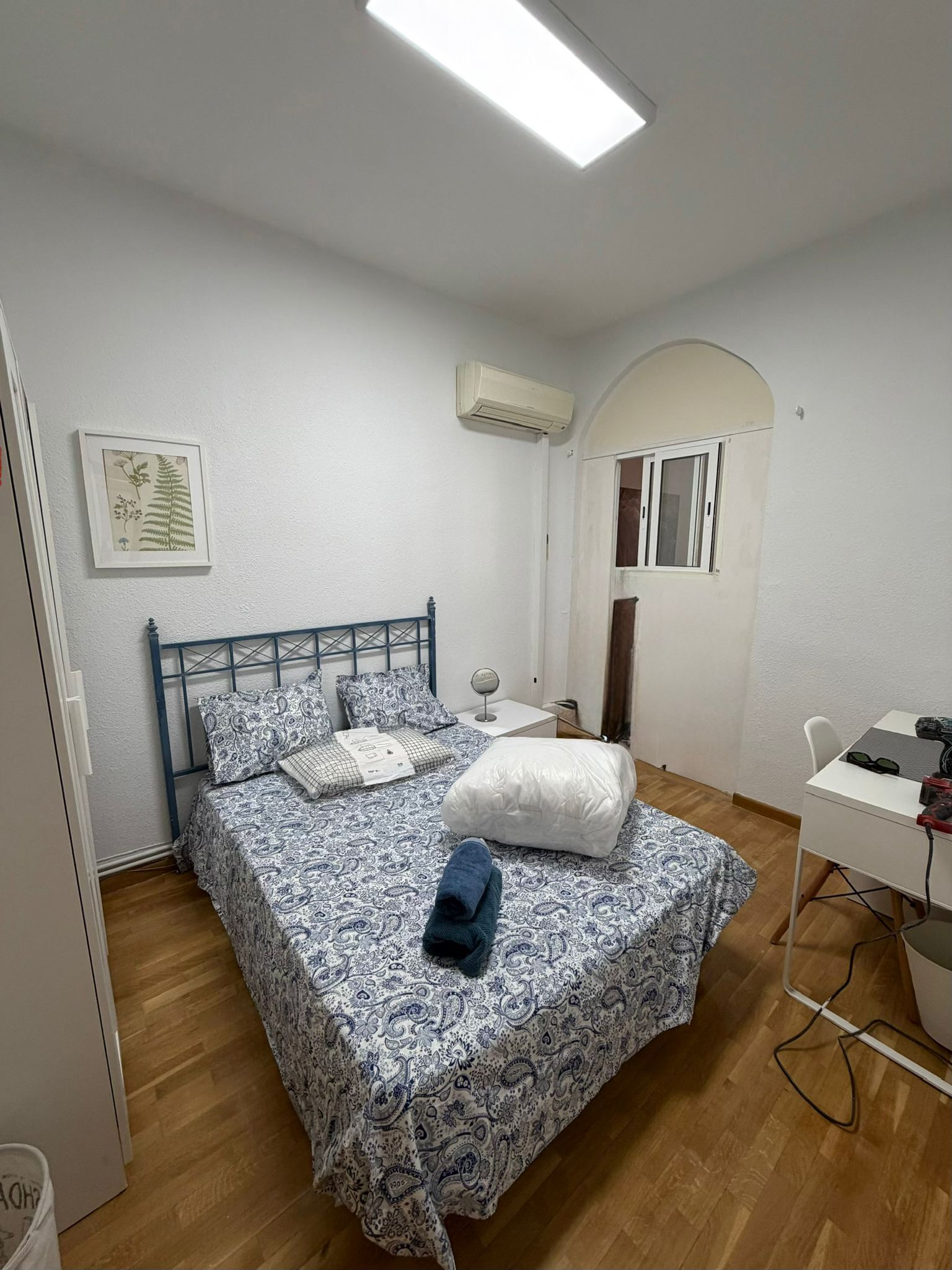 Een slaapkamer met een bed, een bureau, een airconditioner en een raam.