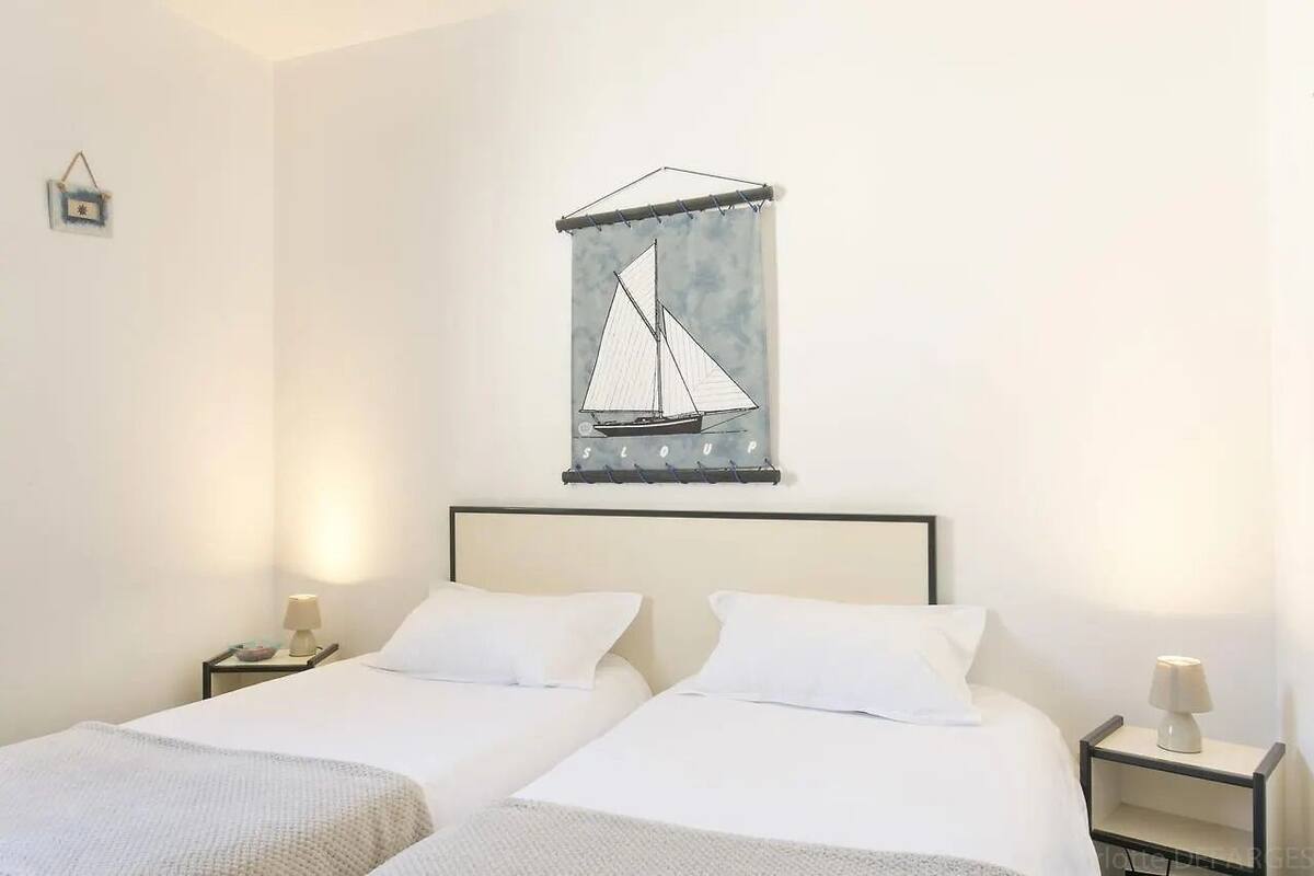 Habitación de hotel con dos camas, una obra de arte de un velero colgado en la pared y lámparas de noche.