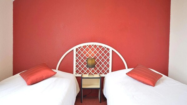 A room with two beds, a white headboard, and a red wall.