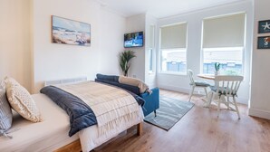 Ett sovrum med en säng, en tv, en växt och en matplats med stolar.