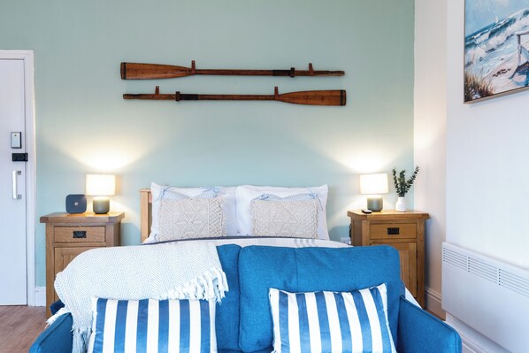 A bedroom with a bed, two bedside tables, a wall-mounted wooden paddle, and a painting of a beach scene.