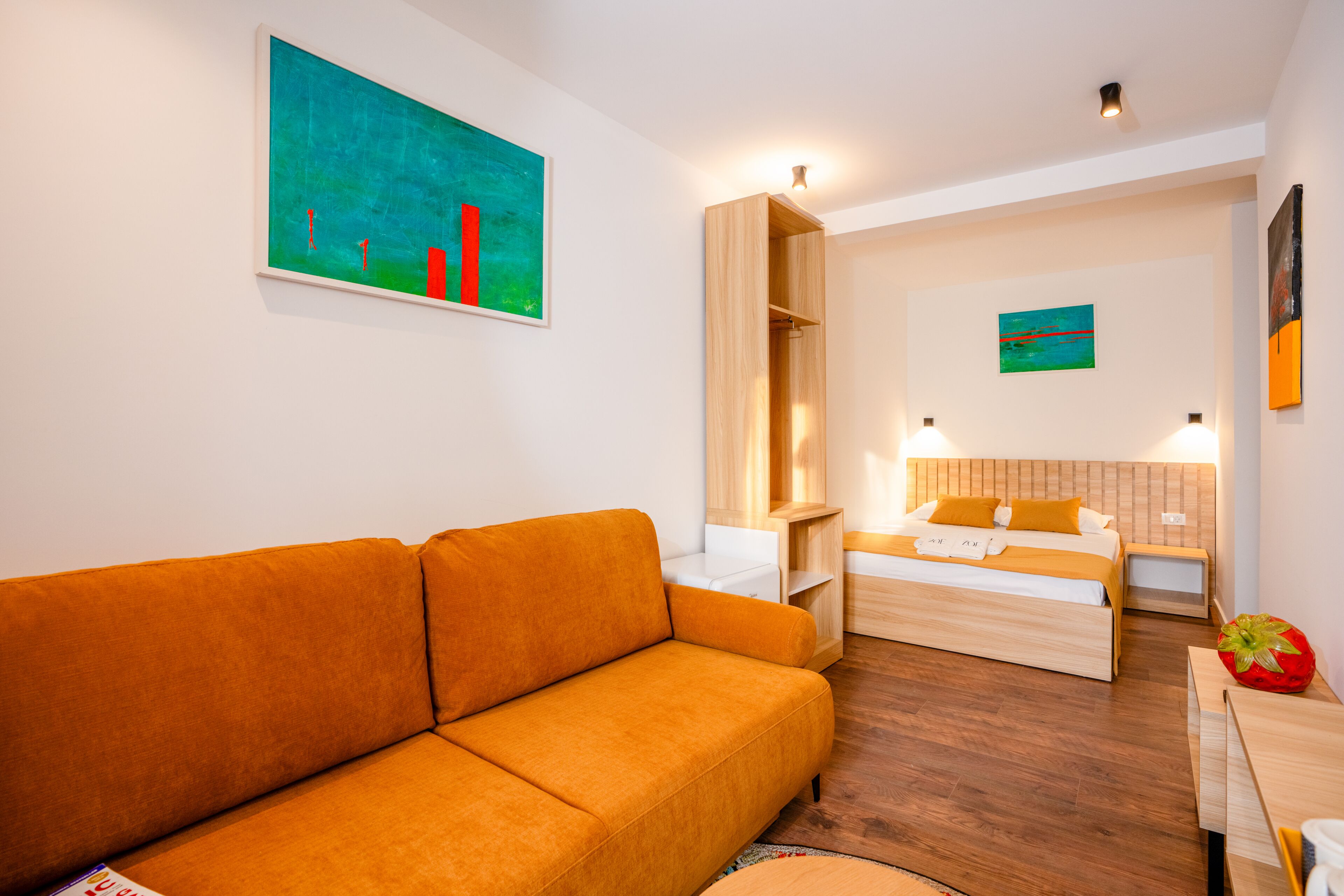 A modern hotel room with a sofa, a bed, a wooden nightstand, and a small table.