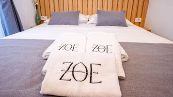 Una cama bien hecha, con toallas que dicen 'ZOE' y un cabecero de madera.