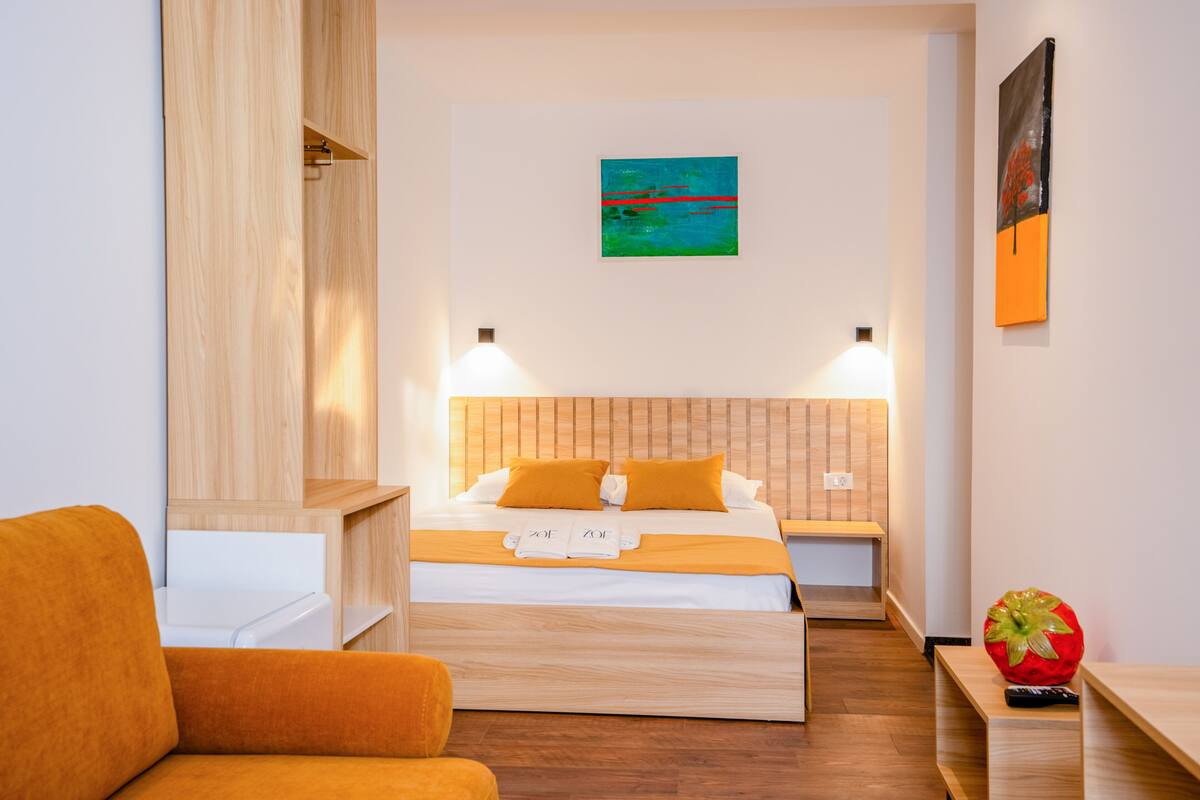 A hotel room with a bed, bedside tables, a sofa, and artwork on the walls.