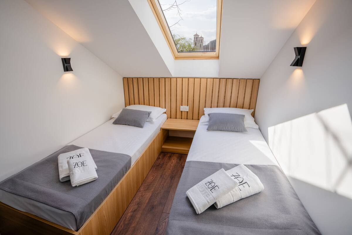 A modern hotel room with two beds, a skylight, and a city view.