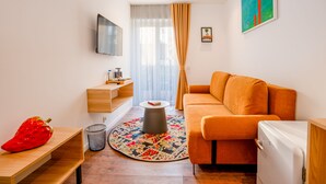 Een moderne woonkamer met een bank, een flatscreen televisie, een klein tafeltje, een prullenbak en een fruitschaal.