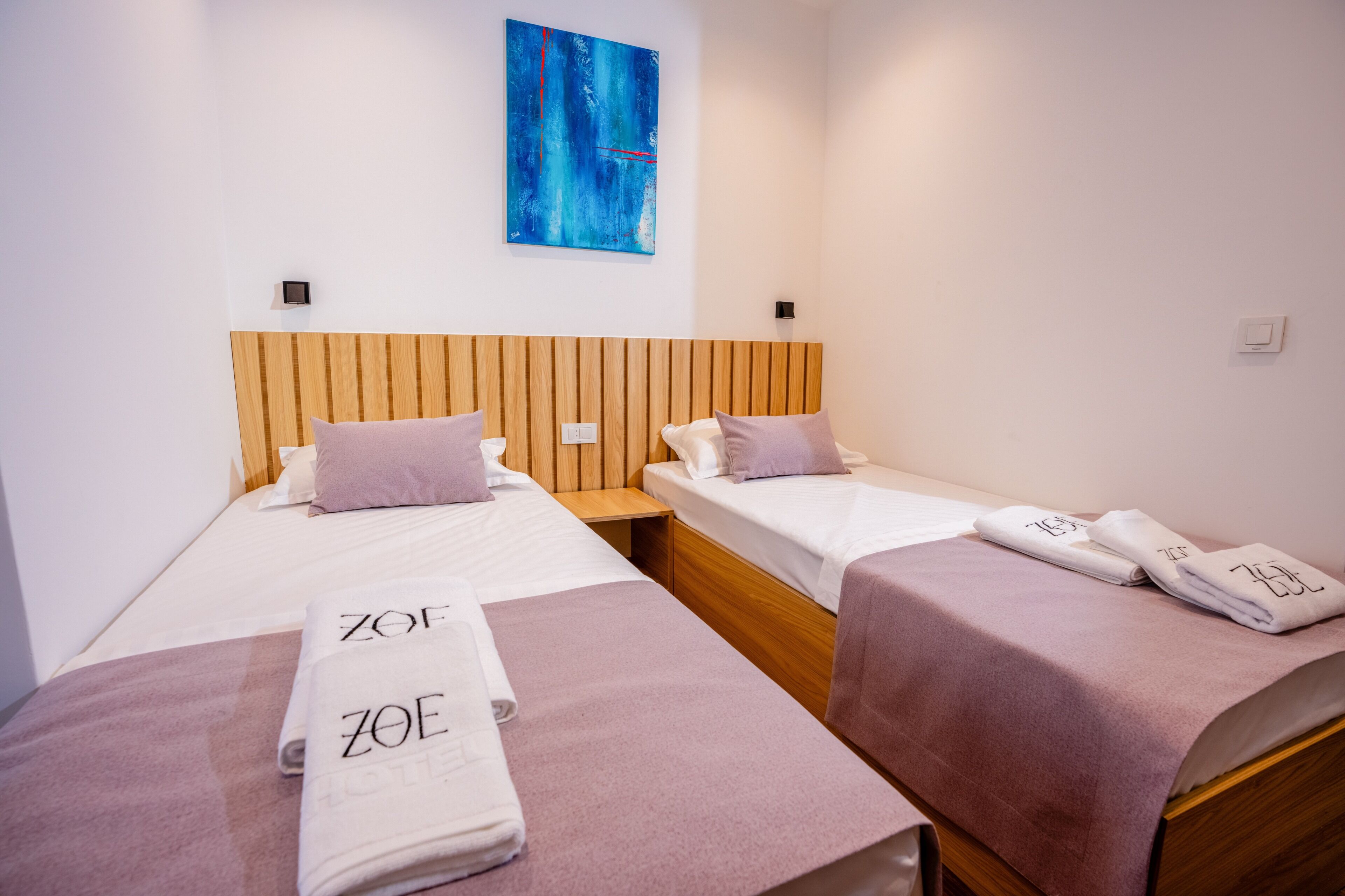 Habitación de hotel con dos camas, cabeceros de madera y toallas con el nombre del hotel.