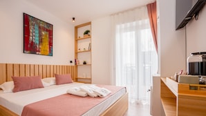 Een moderne hotelkamer met een houten bed, een flatscreen televisie, een koffiezetapparaat en een groot raam met gordijnen.