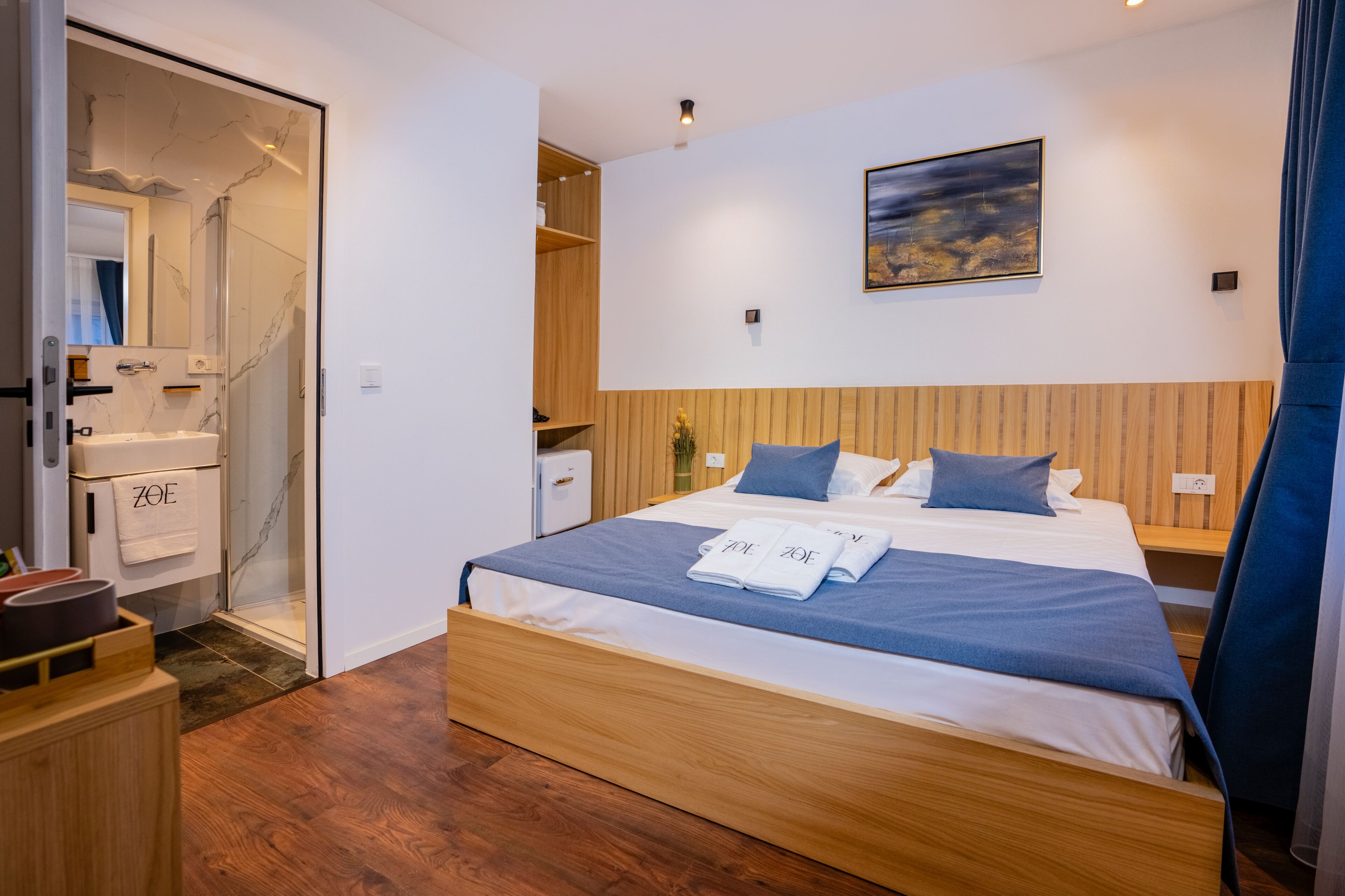 A modern hotel room with a wooden bed, a shower, a small desk, and a painting on the wall.