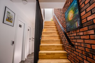 Una escalera con escalones de madera y un muro de ladrillo, que conduce a una habitación con una puerta que dice '103'.