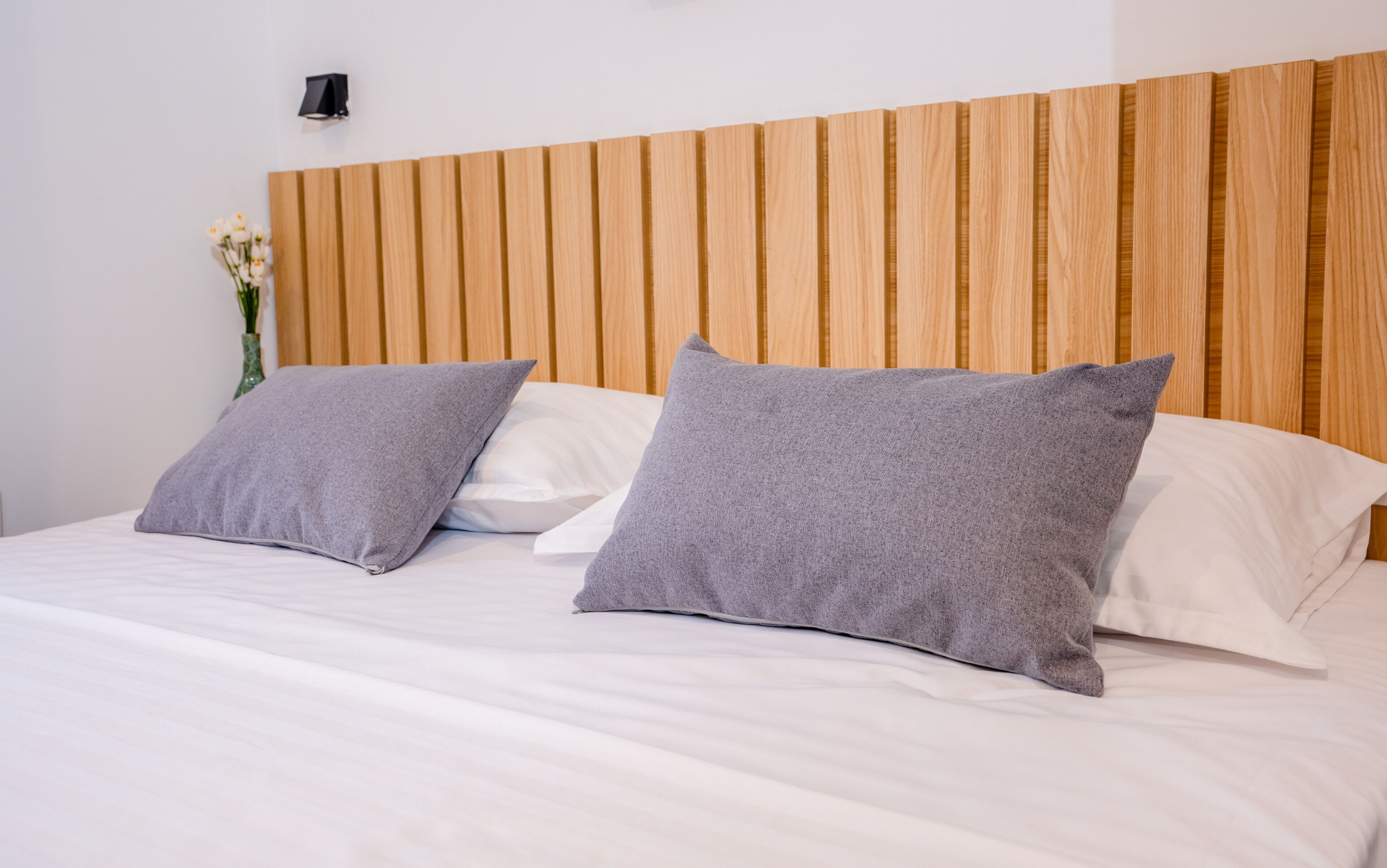 A bed with two pillows, a wooden headboard, and a wall-mounted light fixture.
