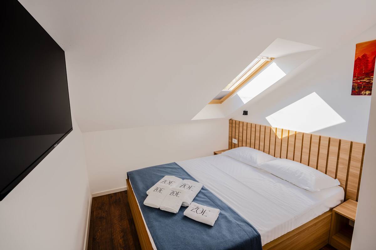 A bedroom with a skylight, a bed with white linens, and a blue bedspread.