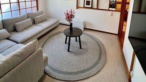 Un salon avec un canapé, une table ronde ornée d’un vase, un ventilateur de plafond et un téléviseur.