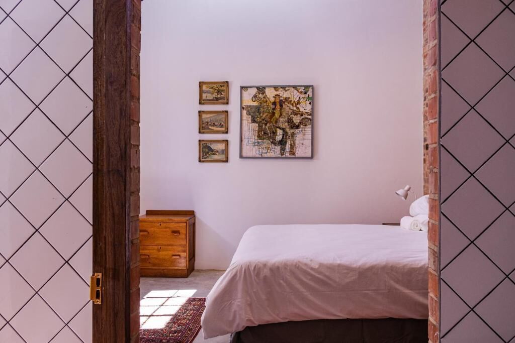 A bedroom with a bed, a wooden chest, and three framed pictures on the wall.