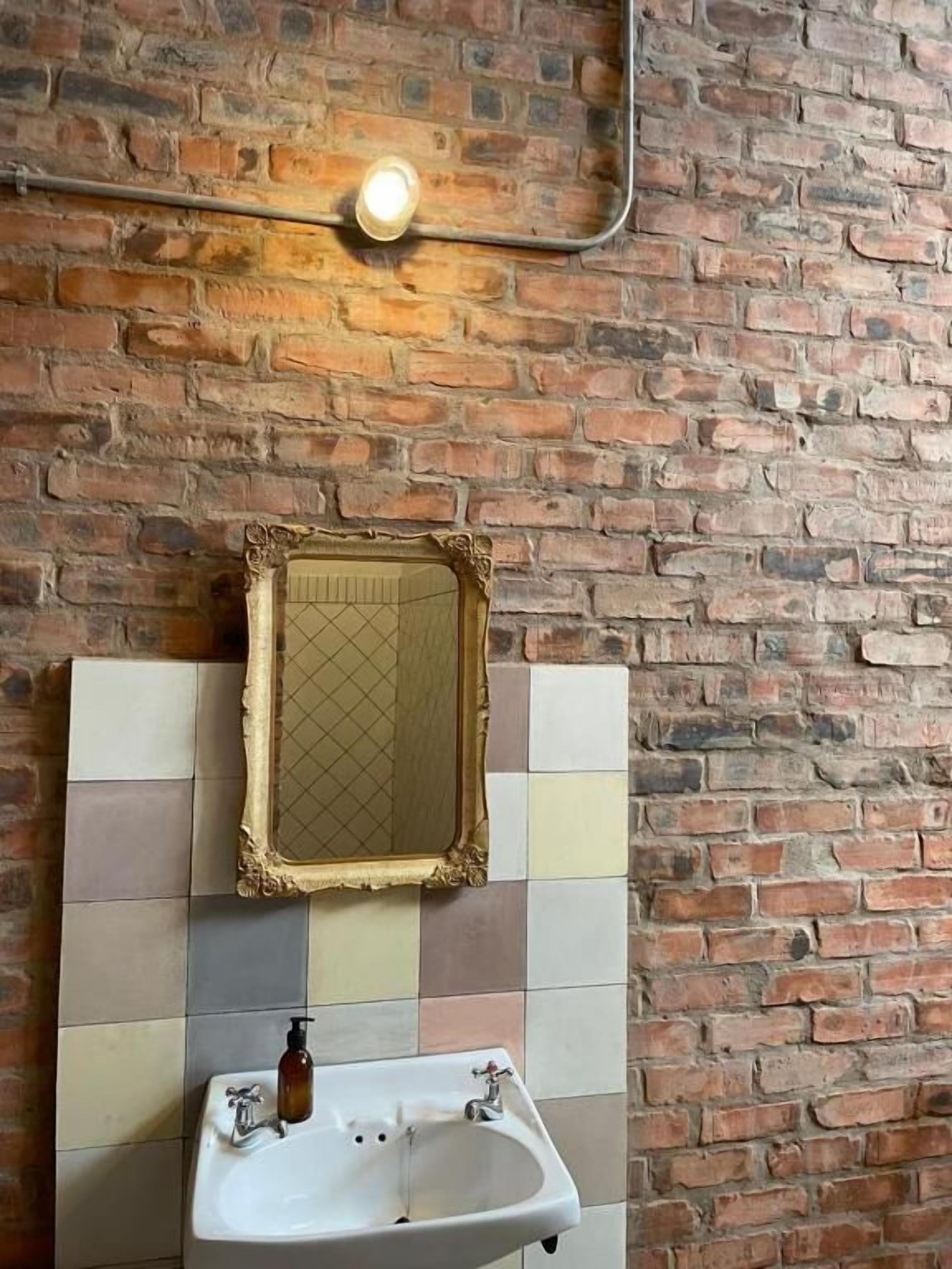 Une salle de bain avec un mur carrelé, un lavabo, un miroir et un luminaire.